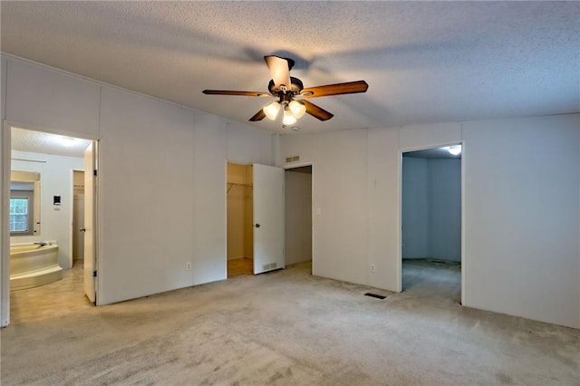 unfurnished bedroom featuring a walk in closet, light colored carpet, ensuite bath, a textured ceiling, and a ceiling fan