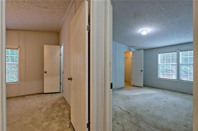 corridor with a textured ceiling and light carpet