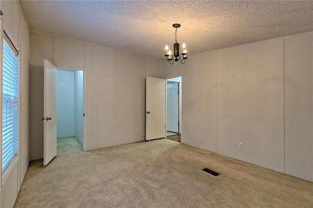 spare room featuring a chandelier, light carpet, and a textured ceiling