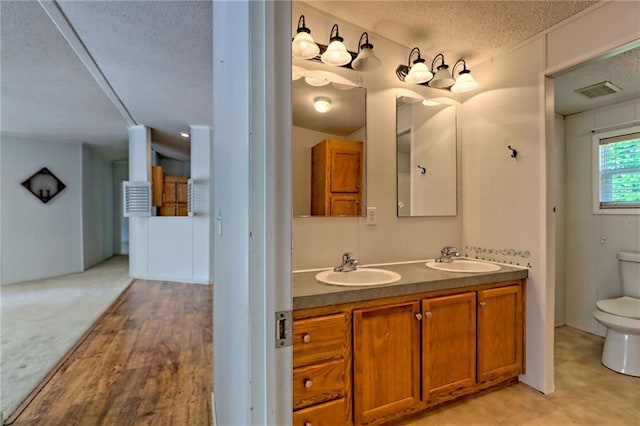 bathroom featuring toilet, a textured ceiling, and double vanity