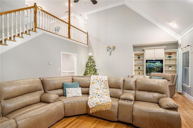 living room featuring ceiling fan, stairway, light wood-type flooring, ornamental molding, and high vaulted ceiling