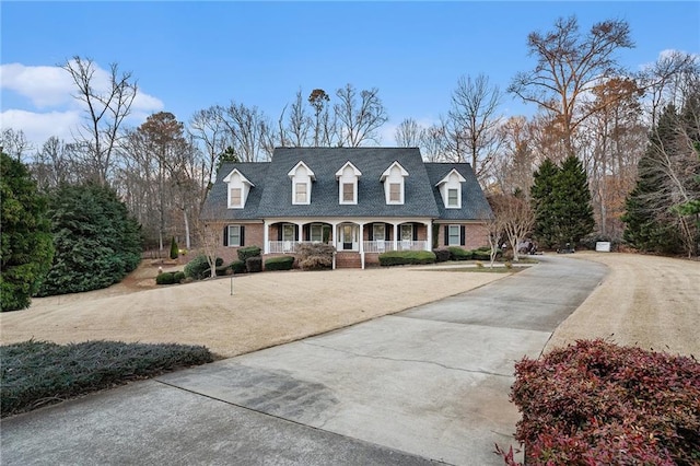 cape cod home featuring concrete driveway, brick siding, and covered porch