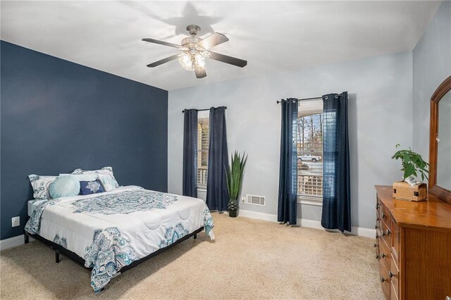 bedroom with visible vents, light colored carpet, baseboards, and ceiling fan