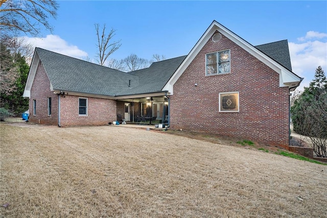 rear view of property featuring a ceiling fan, a lawn, brick siding, and roof with shingles