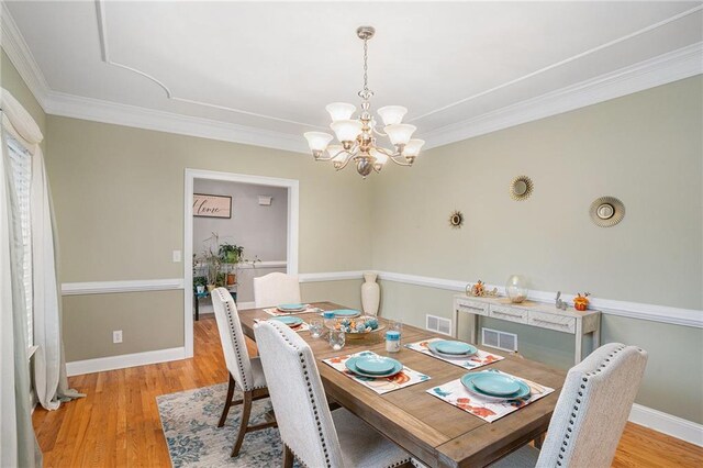 dining space with light wood-type flooring, crown molding, and an inviting chandelier