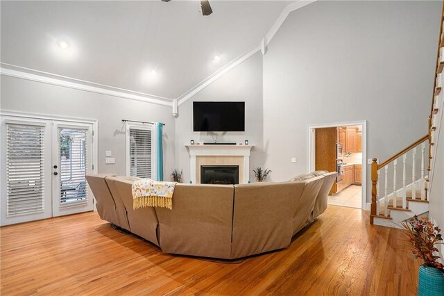 living room with high vaulted ceiling, light hardwood / wood-style flooring, crown molding, and a tiled fireplace