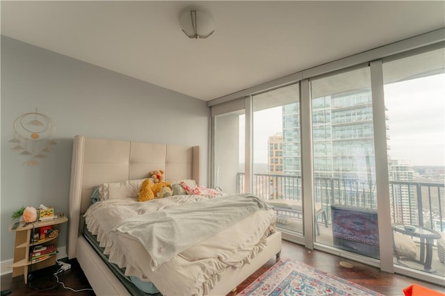 bedroom featuring a city view, wood finished floors, access to exterior, and a wall of windows