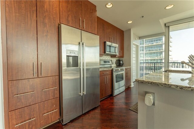kitchen with light stone counters, a sink, appliances with stainless steel finishes, dark wood-type flooring, and recessed lighting
