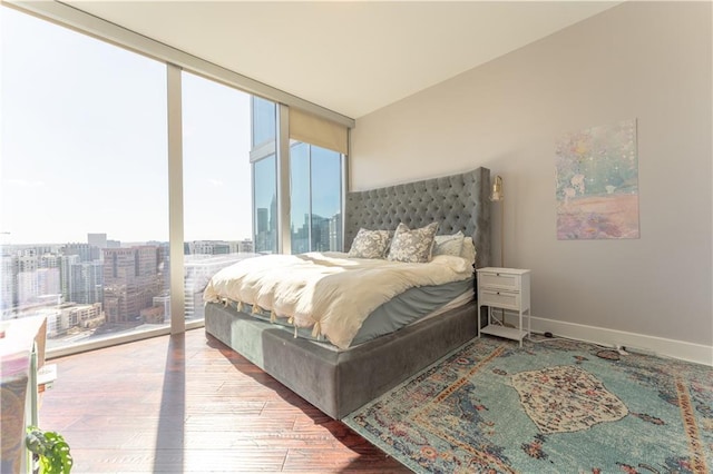bedroom featuring baseboards, floor to ceiling windows, access to exterior, a city view, and wood finished floors