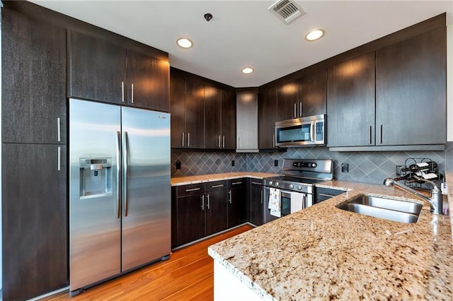 kitchen featuring light stone counters, visible vents, light wood finished floors, a sink, and appliances with stainless steel finishes