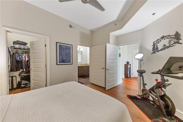 bedroom with wood finished floors, visible vents, ceiling fan, a spacious closet, and connected bathroom