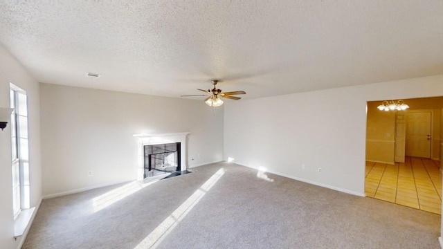 unfurnished living room with a tile fireplace, ceiling fan with notable chandelier, light colored carpet, and a textured ceiling