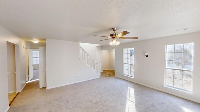 spare room with a textured ceiling, plenty of natural light, light colored carpet, and ceiling fan