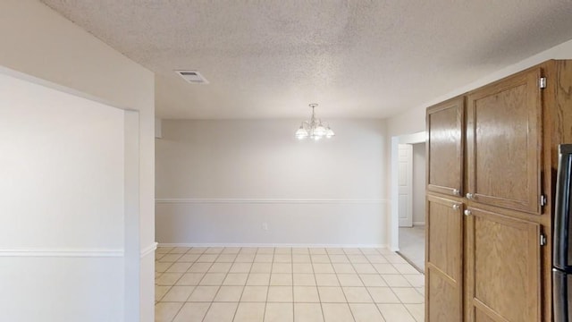 tiled spare room featuring a textured ceiling and a notable chandelier