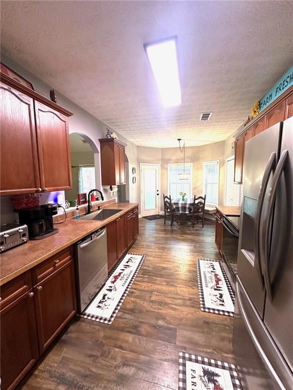 kitchen with sink, dark wood-type flooring, hanging light fixtures, a textured ceiling, and appliances with stainless steel finishes