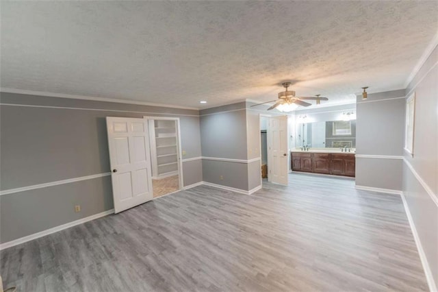 unfurnished room with ceiling fan, ornamental molding, a textured ceiling, and light wood-type flooring