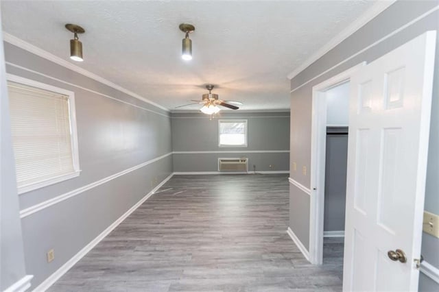 spare room featuring a wall mounted air conditioner, a textured ceiling, ornamental molding, hardwood / wood-style flooring, and ceiling fan