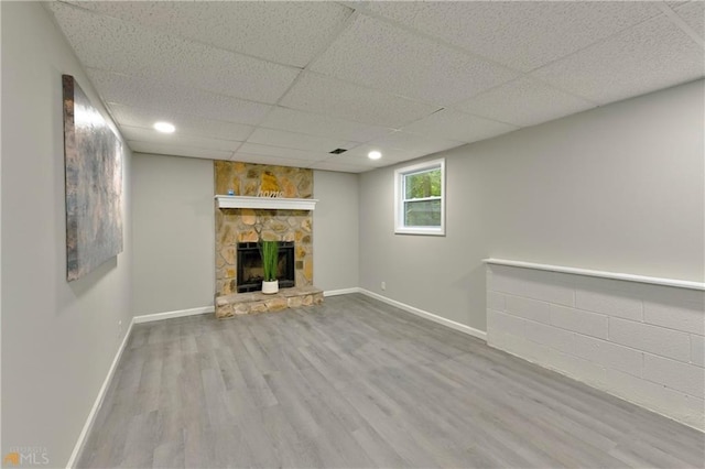 unfurnished living room with a paneled ceiling, a stone fireplace, and hardwood / wood-style floors