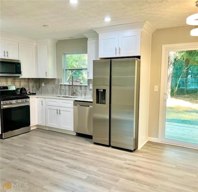 kitchen featuring light hardwood / wood-style floors, white cabinetry, appliances with stainless steel finishes, backsplash, and sink