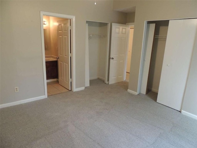 unfurnished bedroom with light carpet, connected bathroom, and multiple closets