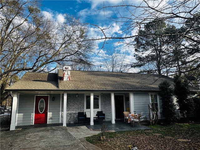 ranch-style house featuring stone siding, a shingled roof, a chimney, and a porch