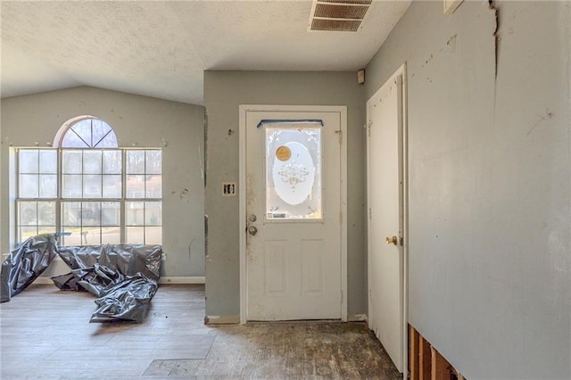 entrance foyer with lofted ceiling, visible vents, a textured ceiling, and wood finished floors