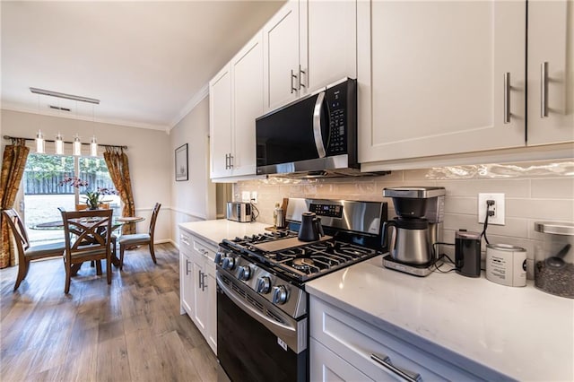 kitchen with white cabinets, appliances with stainless steel finishes, wood finished floors, crown molding, and backsplash