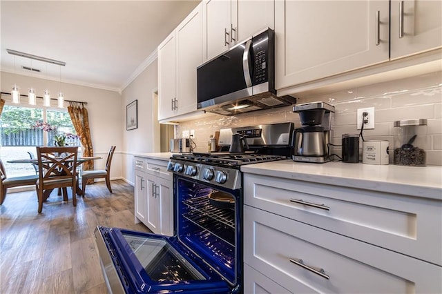 kitchen featuring tasteful backsplash, white cabinets, ornamental molding, wood finished floors, and stainless steel appliances