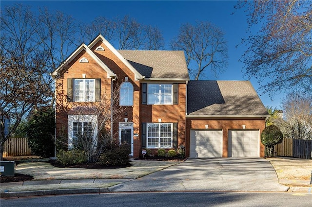 colonial inspired home with driveway, roof with shingles, an attached garage, fence, and brick siding