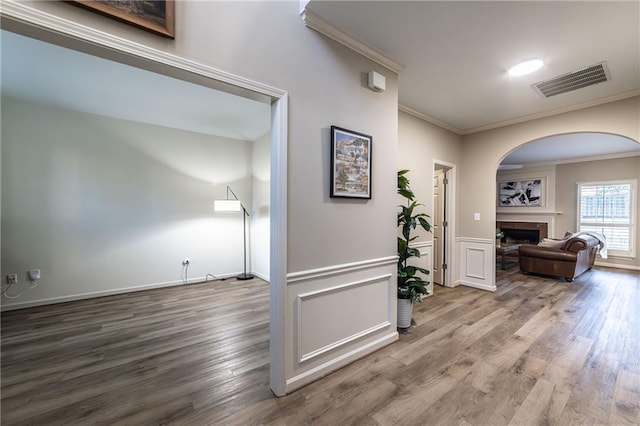 corridor with ornamental molding, a wainscoted wall, visible vents, and wood finished floors