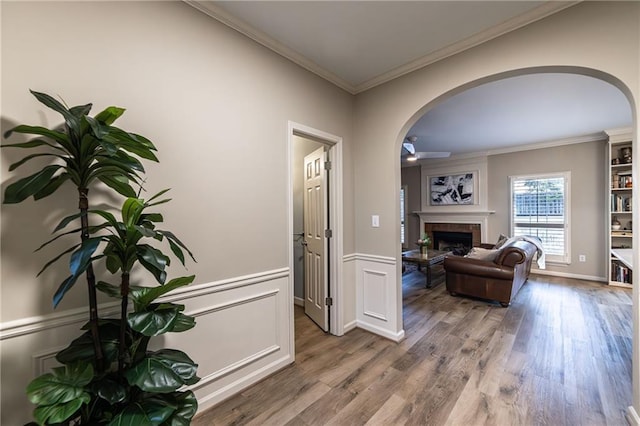 interior space featuring arched walkways, ornamental molding, a wainscoted wall, and wood finished floors