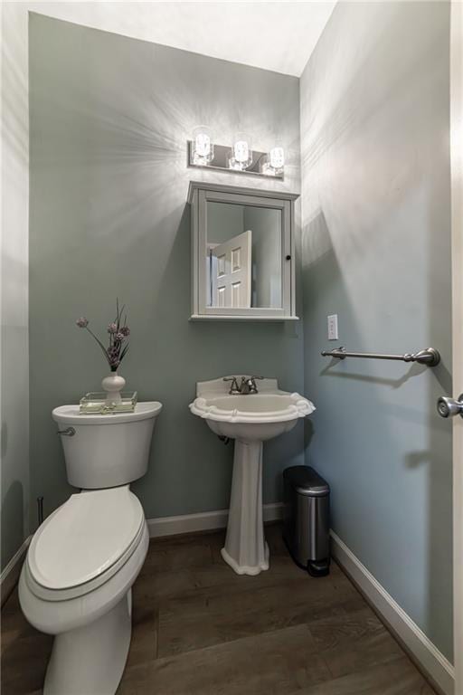 half bathroom with wood finished floors, toilet, and baseboards