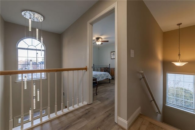 hallway with baseboards, wood finished floors, a wealth of natural light, and an upstairs landing