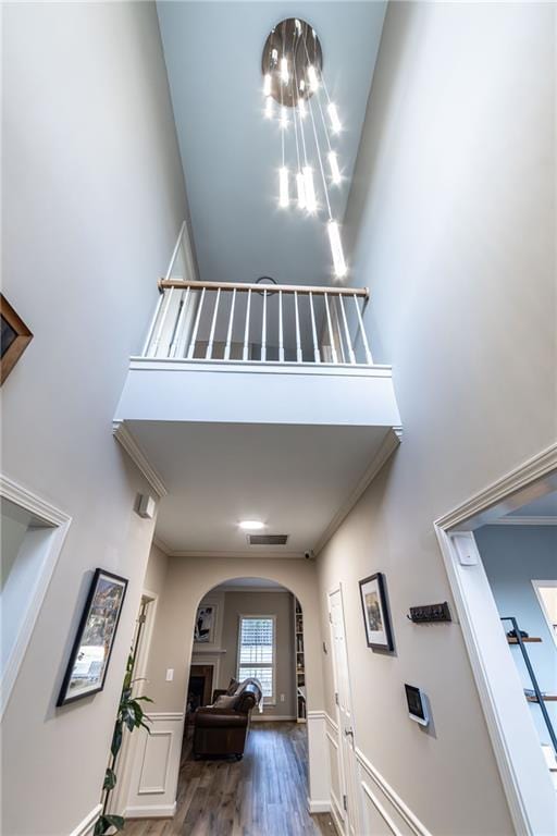 hall with arched walkways, crown molding, visible vents, a high ceiling, and wood finished floors