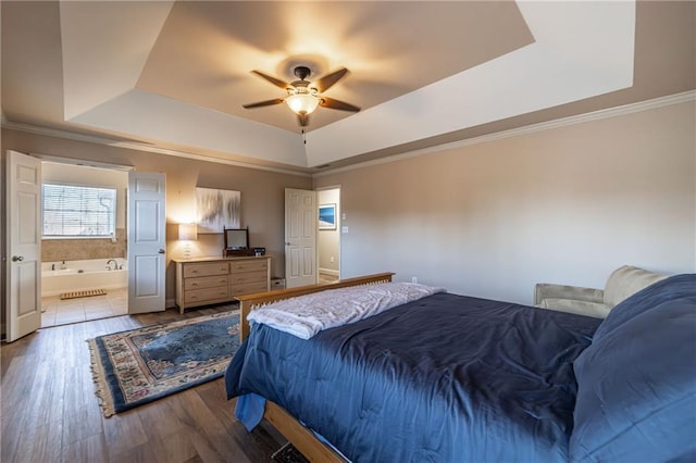 bedroom with connected bathroom, a tray ceiling, crown molding, and wood finished floors