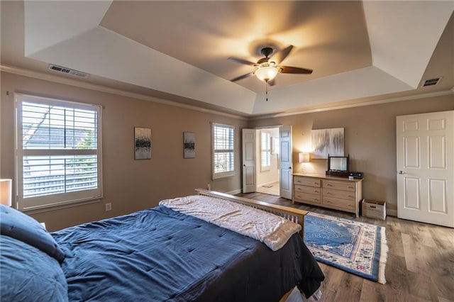 bedroom featuring ornamental molding, wood finished floors, a raised ceiling, and visible vents