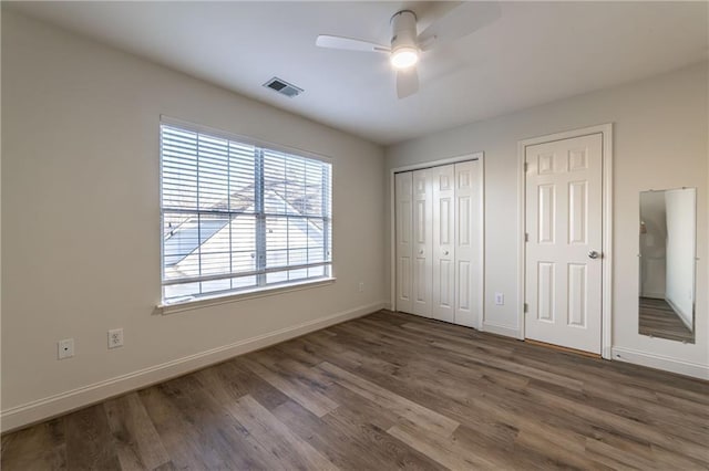 unfurnished bedroom with two closets, visible vents, a ceiling fan, wood finished floors, and baseboards