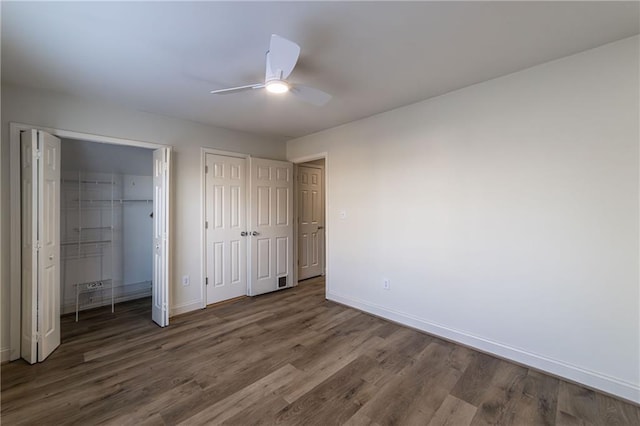 unfurnished bedroom featuring ceiling fan, wood finished floors, two closets, and baseboards