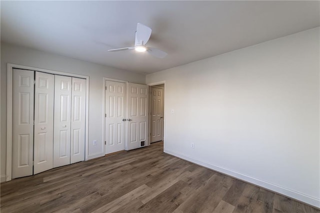 unfurnished bedroom with a ceiling fan, wood finished floors, baseboards, and two closets