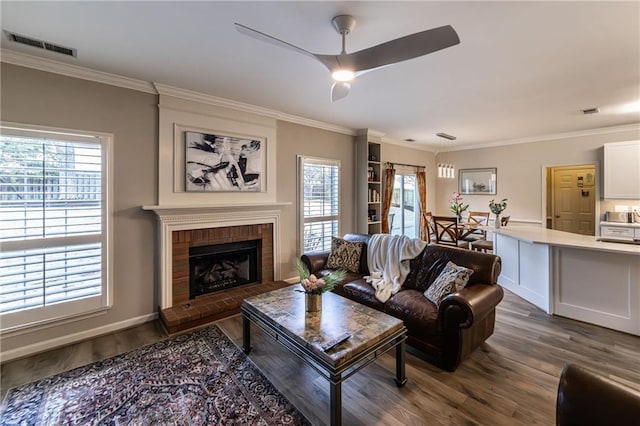 living area with ornamental molding, a brick fireplace, visible vents, and dark wood finished floors