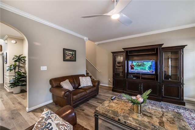 living room with baseboards, arched walkways, a ceiling fan, ornamental molding, and wood finished floors