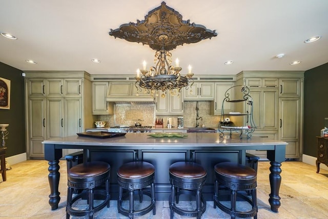 kitchen with a notable chandelier, tasteful backsplash, a kitchen bar, and an island with sink