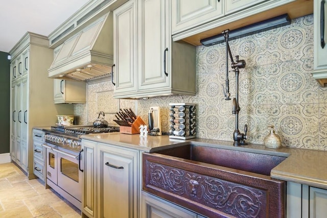 kitchen with custom range hood, backsplash, range with two ovens, and light tile flooring