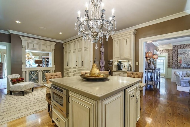 kitchen featuring an inviting chandelier, light hardwood / wood-style floors, a kitchen island, pendant lighting, and cream cabinetry