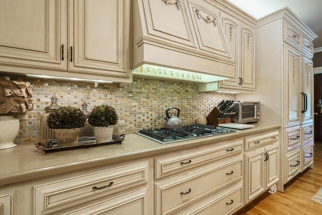 kitchen with backsplash, cream cabinetry, light hardwood / wood-style flooring, and stainless steel gas stovetop