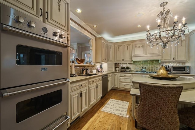 kitchen with appliances with stainless steel finishes, pendant lighting, an inviting chandelier, tasteful backsplash, and light hardwood / wood-style flooring