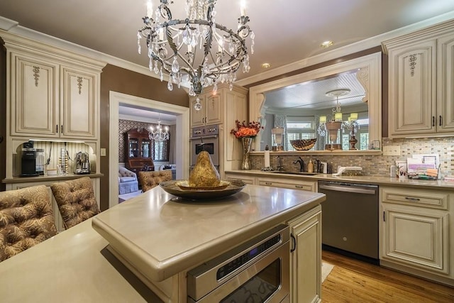 kitchen with an inviting chandelier, appliances with stainless steel finishes, light wood-type flooring, a center island, and ornamental molding