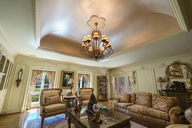 living room with ornamental molding, a notable chandelier, hardwood / wood-style floors, and a tray ceiling