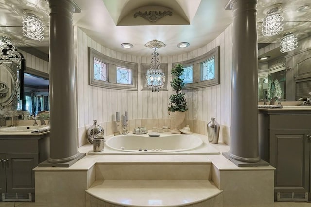 bathroom with an inviting chandelier, oversized vanity, dual sinks, ornate columns, and a relaxing tiled bath