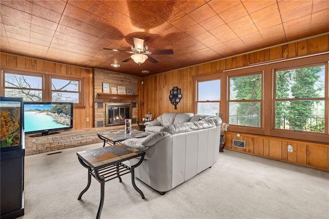 carpeted living area featuring a healthy amount of sunlight, wood walls, and a glass covered fireplace